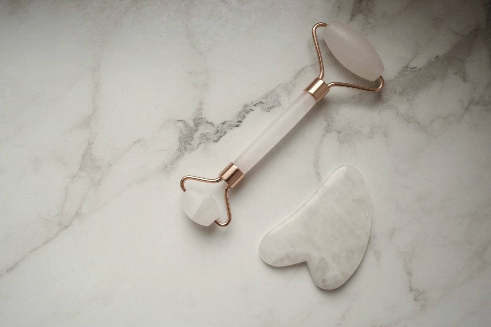 Açık mermer üstünde yüz masaj rulosu ve gua sha taşı