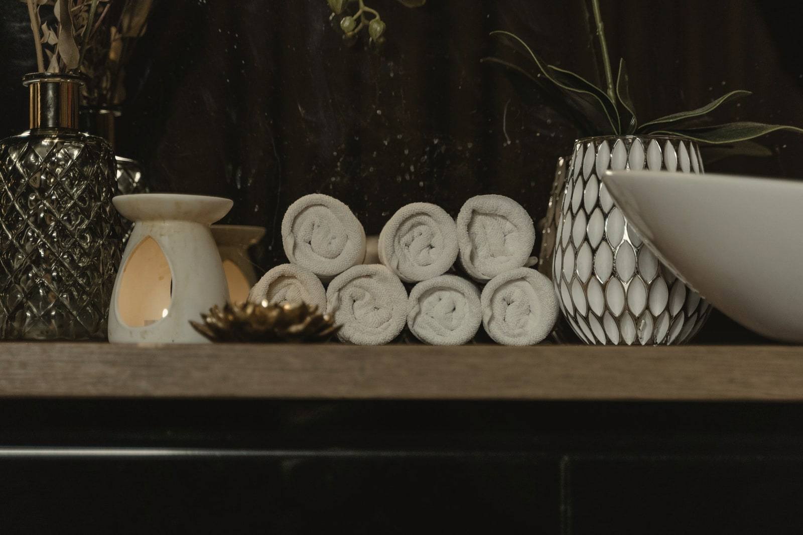 Rolled towels, a lit candle and a ceramic bowl on a wooden shelf
